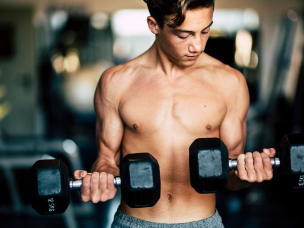 rapaz realizando exercício para o músculo bíceps braquial em uma sala de musculação