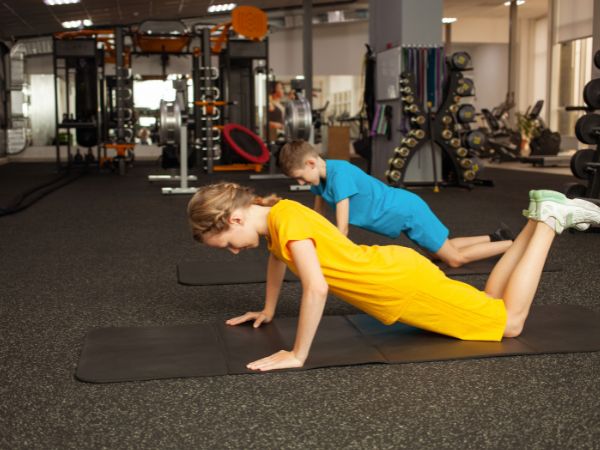 crianças fazendo flexões de braços em academia com área kids